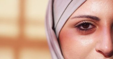 Kafası kapalı, kahverengi gözlü, yetişkin Arap kadın yüzüne yakın çekim. Mor tesettürlü güzel Müslüman kadın kameraya bakıyor ve göz kırpıyor. Feminizm, din, insan kavramı.