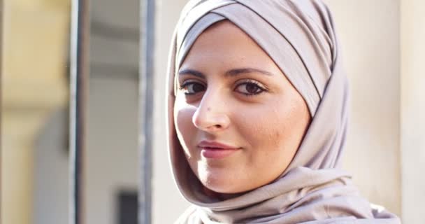 寺院の近くの通りを歩いて覆われた頭を持つ若い女性のアラブ人の肖像画 ピンクのヒジャーブを身に着けているイスラム教徒の女性は屋外でカメラと笑顔 宗教人権の概念 — ストック動画