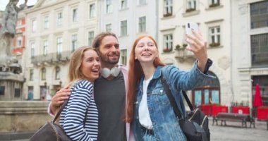 Şehirde akıllı telefondan video çeken üç erkek ve kadın en iyi arkadaş. Genç öğrenciler fotoğraf çekiyor, gülümsüyor ve gülüyorlar. Teknoloji, arkadaşlık, aletler konsepti.