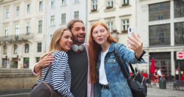 Beyaz gençler şehirdeki caddede akıllı telefondan fotoğraf ve video çekiyorlar. Güzel kızlar ve kameraya doğru kıvrılıp dışarıda gülen bir adam. Teknoloji, gençlik, eğlence konsepti.