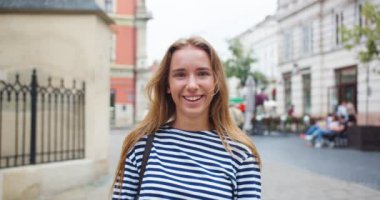 Eski şehirde sokakta duran çekici bir kadının portresi. Sırt çantalı, kameraya bakıp gülümseyen beyaz bir kadın. Mutluluk, gençlik, güzellik konsepti.