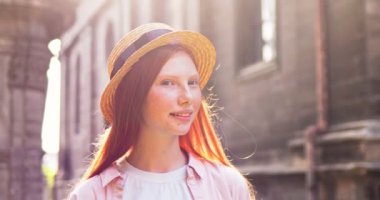 Eski binanın yakınındaki caddede duran şapka takan çekici kadın turistin portresi. Kafası çilli genç beyaz kadın kameraya bakıyor ve gülümsüyor. Seyahat, kültür konsepti.