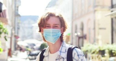 Dışarıda tıbbi koruyucu maske takan beyaz bir adamın portresi. Yakışıklı bir erkek kameraya bakıp sokakta gülümsüyor. Coronavirus, covid-19, sağlık, güvenlik, salgın konsepti.