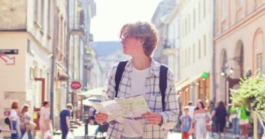 Yakışıklı turist sokakta dolanıp binalara bakıyor. Sırt çantalı beyaz gözlüklü genç adam yön bulmak için kağıt harita kullanıyor. Seyahat, turizm konsepti.