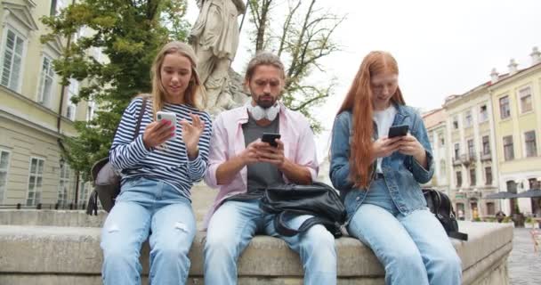 Studentinnen Und Männliche Studenten Sitzen Auf Bänken Und Verwenden Kommunikationsgeräte — Stockvideo