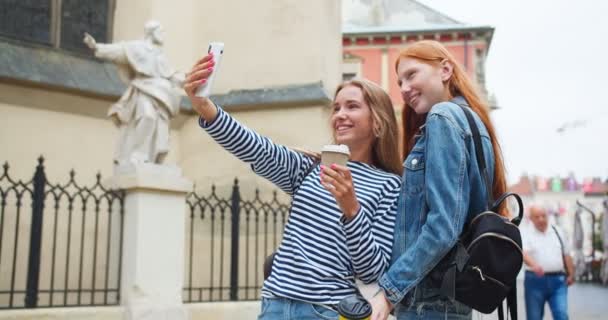 两个漂亮的女孩站在街上拍照 扭来扭去拍照 红头发的女人和她的朋友在城里摆姿势 微笑着拍照 Hype Social Media — 图库视频影像