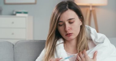 Hasta, Kafkasyalı, kötü görünümlü genç bir kadının battaniyeyle evinde oturması ve vücut ısısını ölçmesi. Grip ya da koronavirüsünün ateşi olan hasta bir kız. Corona belirtileri olan bir kadın..