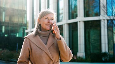 Portre başarılı, emekli, modaya uygun, dışarıda yürüyen, akıllı telefondan konuşan bir kadın..