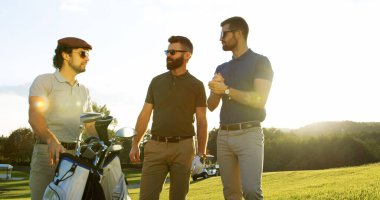 Portrait of three attractive men talking and holding the golf bag on the nice sunny day on the golf pitch