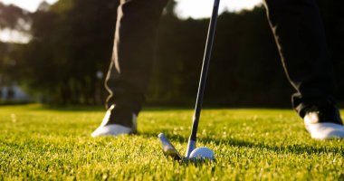 Close up of a moment when ball being strongly hitted by a club on the green golf pitch on a sunny summer day rising grass up.