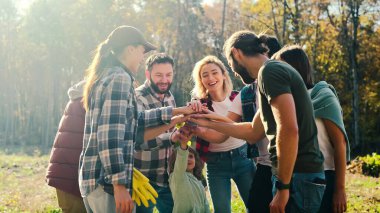 Caucasian team of males and females, volunteers with child putting hand on hand in circle and making gesture of cooperation and coworking. Successful work together concept. Eco activists. Outdoors.