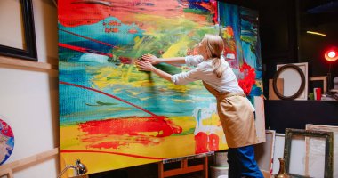 Rear of emotional Caucasian young innovative professional woman artist working in workshop at night and drawing on big canvas with her hands creating abstract art piece, creative work, hobby concept