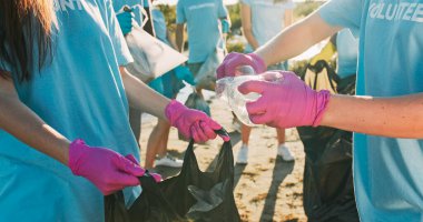 Güzel beyaz kadın gönüllüler çöp torbasında çöp topluyor. Eldivenli genç kadın çevreciler plastik şişe bastırıyor, kameraya bakıyor ve gülümsüyor. Geri dönüşüm, kirlilik kavramı.