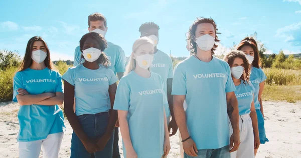 Multiracial group of volunteers concerned about the environmental problems. Active conservationists in medical masks standing and looking at camera. Nature protection, healthcare concept.