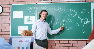 Kafkasyalı küçük okul çocuğu kimya erkek öğretmenine tahtadan cevap veriyor ve kimyasal formüller yazıyor. Okul konseptinde dersler. Çocuklar için eğitim. Sınıftaki öğrencilerin arkası..