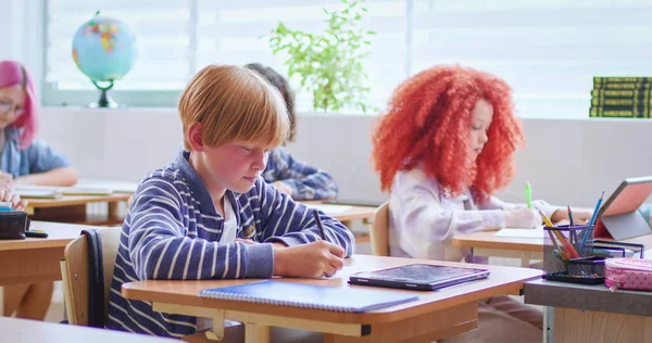 白人の賢い10代の少年は教室の机に座ってコピーブックに書いている 学校のコンセプトで勉強する レッスンで学ぶ賢い少年はテストに合格し集中している — ストック写真
