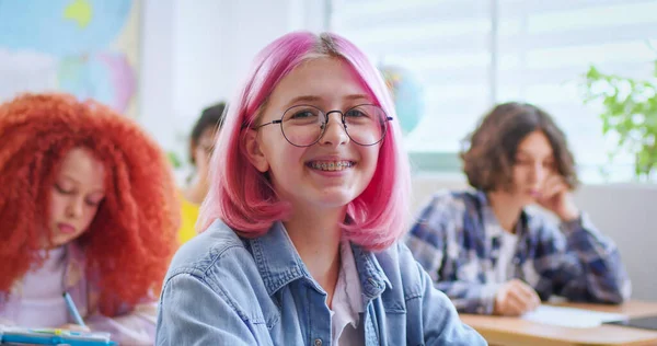 Szczęśliwa Nastoletnia Biała Dziewczyna Okularach Różowymi Włosami Siedząca Przy Biurku — Zdjęcie stockowe