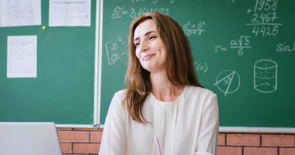 Beautiful Caucasian young female teacher explaining math and answering to pupils at blackboard. Mathematics lesson. Pretty woman master educating kids. Education concept. School.