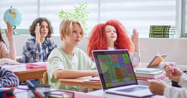学生们在听老师提问时 坐在办公桌前 用的是现代笔记本电脑 在明亮的教室里 高举双手准备上课时回答问题的学生 — 图库照片