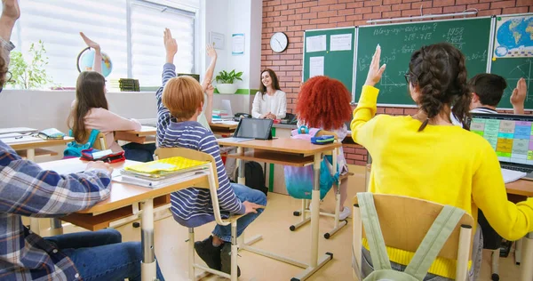 学生们坐在课桌前的倒影 老师问的时候举手 孩子们在学校的背影 班级概念 教育儿童的年轻教师 — 图库照片