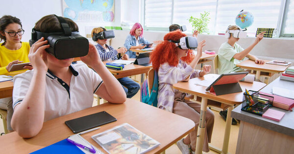Smart pupils wearing VR headsets and studying with future technologies at classroom. Excited boys and girls in virtual glasses experienced augmented reality at lesson in school.