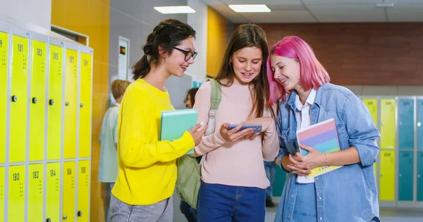 三位学龄朋友在课间休息时用智能手机 白种人微笑的女学生下课后一起在走廊里用手机上网 — 图库照片
