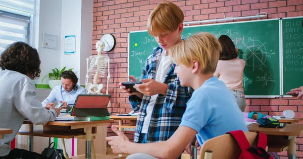 两名高加索少年学生在学校课间休息时玩智能手机和聊天 朋友们一边玩手机一边聊天 上学的生活 — 图库照片