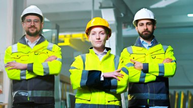 Kafkaslı erkek ve kadın meslektaşlarının kamera karşısında el ele tutuşan kask ve üniforma imalatındaki portreleri. Fabrikadaki erkek ve kadın iş arkadaşları. Fabrika işçileri takımı.