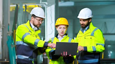 Manufactory 'daki beyaz erkek ve kadın meslektaşlar dizüstü bilgisayarla iş konuşuyorlar ve tartışıyorlar. Üretim tesisi. İçeride. Fabrikadaki erkek ve kadın iş arkadaşları. İnşaat alanı. İnşa edenler.