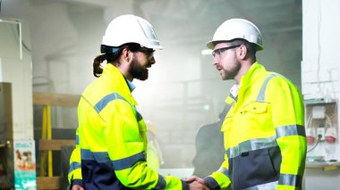 Fabrikada üniformalı, miğferli ve gözlüklü işçi arkadaşları buluşup el sıkışıyorlar. Selamlama işareti. İçeride. Fabrikadaki meslektaşlarım iş hakkında konuşuyor..