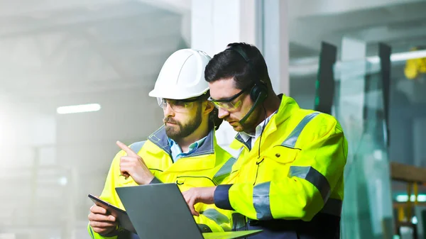 stock image Caucasian male technician in headset and uniform standing in factory, talking with video and working at laptop. Producing concept. Indoor.