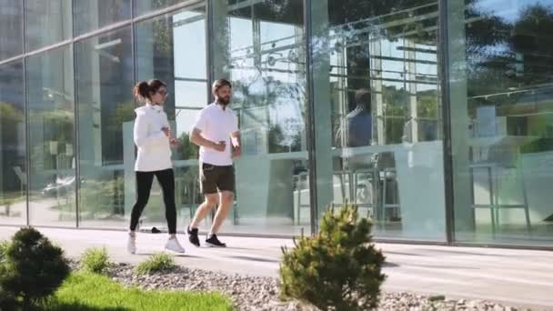 Glada Vänner Sportkläder Som Löper Längs Glasväggen Kontorsbyggnad Stan Ung — Stockvideo