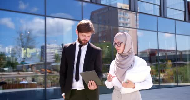 英俊的白人商人老板和年轻的阿拉伯穆斯林女助手一起走在街上 展示平板设备方面的重要工作 忙着工作的人 — 图库视频影像