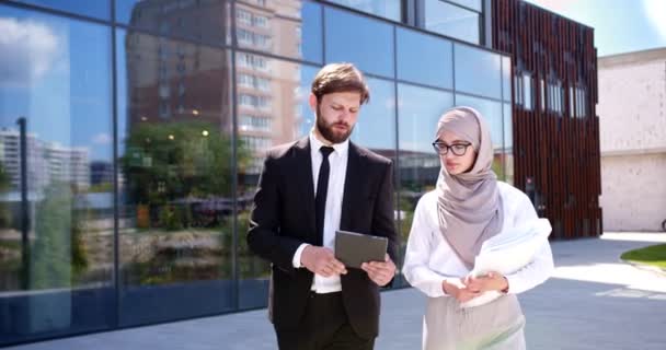 高加索商人老板与年轻的阿拉伯穆斯林女助手一起走在户外 展示平板设备方面的重要工作 忙碌的同事忙着工作 平等权利 — 图库视频影像
