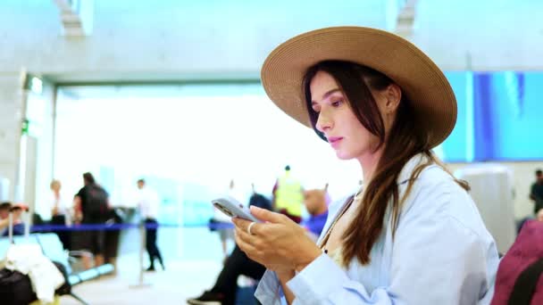 Νεαρή Ελκυστική Ευχάριστη Καυκάσια Γυναίκα Κάθεται Στο Αεροδρόμιο Κοιτάζοντας Smartphone — Αρχείο Βίντεο