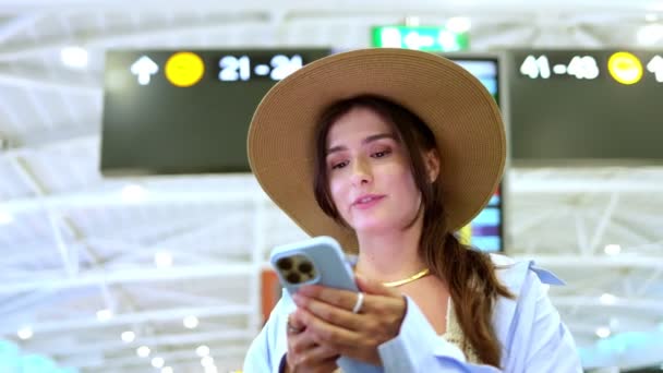 快乐迷人的年轻白人女人站在机场 微笑着等待着 漂亮可爱的女孩在网上使用社交媒体的智能手机等待飞行 旅行概念 — 图库视频影像