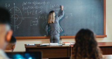 Lisedeki beyaz kadın profesör öğrencilere matematik anlatırken tahtaya yazı yazıyor. Üniversite bilgisi. Kadın öğretmen matematik formüllerini ve öğretmenliği anlatıyor..