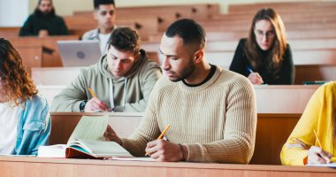 Üniversitede ders dinleyen, ders kitabı yazan ve kullanan yakışıklı Afrikalı bir erkek öğrenci. Lisedeki seminerde kitap okuyor. Üniversite konsepti. Çalışan adam