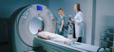 Young man lies down in MRI capsule. Chief head doctor in dressing gown hold folder and explains to patient what to do. Nurse monitors process of examiming. Man undergoes magnetic resonance imaging. clipart