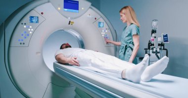 Hasta MRI testi için hazırlanıyor. İnsan MRI kapsülüne giriyor. Kadın doktor hastayı sakinleştirir ve manyetik rezonans görüntülemesi yapar. Sağlık görevlisi MRI kapsülündeki düğmelere basıyor..