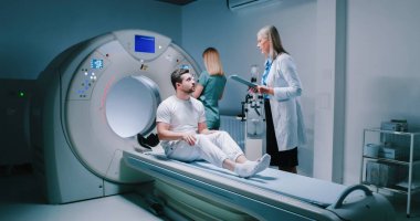 Erkek hasta taranmayı bekliyor. Adam kadın doktorla konuşuyor. Hemşire manyetik rezonans tomografisi için hazırlanıyor. Hasta MRI incelemesi için hazırlanıyor..