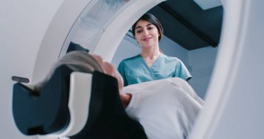 Female finished magnetic resonance imaging, Patient is moving out of MRI scanner capsule. Female doctor asks patient about well-being after examining. Doctor is smiling and have talk with woman. clipart