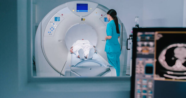 Медсестра отправила пациента на МРТ-капсулу на столе. Магнитно-резонансная томография мозга. Зал осмотра с медицинским оборудованием.