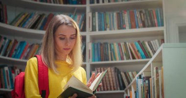 Kütüphanede durmuş kitap okuyan beyaz, güzel, sarışın bir kız öğrenciyi yakından çek. Akıllı bir kadın İncil 'de ders kitabı okur. Kendini eğitiyorsun. Öğrenme konsepti. Edebiyat.