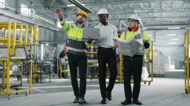 Kasklı üç mühendisin portresi konuşuyor. Sakallı, beyaz bir erkek, elinde yepyeni bir laptop var. Çizimi olan kısa boylu Asyalı adam. Afro-Amerikalı erkek jestler yapıyor..