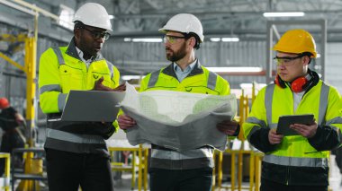 Erkek endüstriyel mühendisler birbirleriyle iletişim kurarlar. Fabrika işçileri yeni proje yapmak için cihazlar ve planlar kullanıyorlar. İnşaat alanındaki çok kültürlü çalışanların işbirliği.