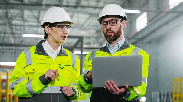 头戴硬礼帽 身穿黄色背心的男女工业家在使用笔记本电脑的同时讨论新项目 员工们正在建筑工地进行交谈和准备 讲习班上的团队精神 图库图片