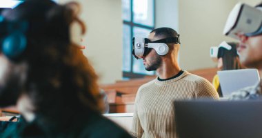 VR gözlüklü, üniversitede ders çalışan ve sağa sola dönen çok ırklı erkek ve kız öğrencilere yakın durun. Yüksek teknoloji çalışması. Teknolojik eğitim yöntemlerini öğrenen melez gençler.