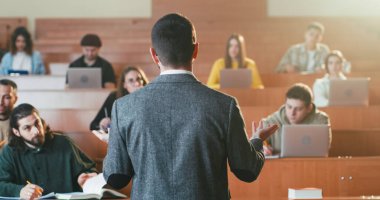 Arkadan bak. Lisede okutman. Arkaplanda öğrenciler.