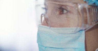 Tıbbi maskeli ve gözlüklü kadın epidemiyolojistin portresi başka tarafa bakıyor. Tam koruma kostümü giymiş laboratuvar asistanının yan görüntüsü. Kafkasyalı sağlık görevlisi kameraya bakıyor..